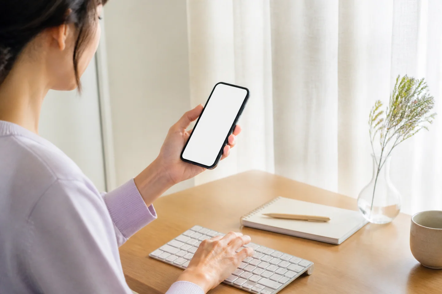 パソコンで文章を入力しながらスマートフォンを確認する女性